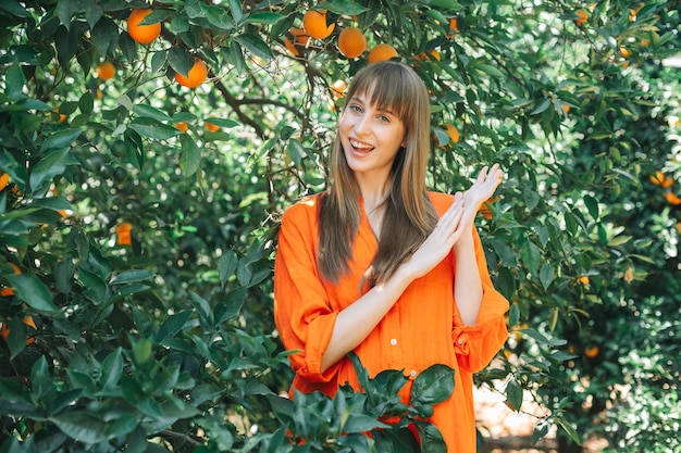 Lachend meisje in oranje jurk poseert voor de camera door elkaars hand vast te houden in de oranje tuin