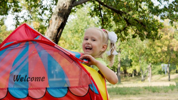 Lachend schattig klein blond meisje turen over de bovenkant van een kleurrijke tent buiten in het park