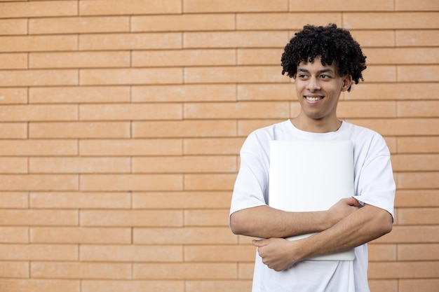 Lachende Afro-Amerikaanse man die een gesloten laptop vasthoudt en wegkijkt en een wit t-shirt draagt