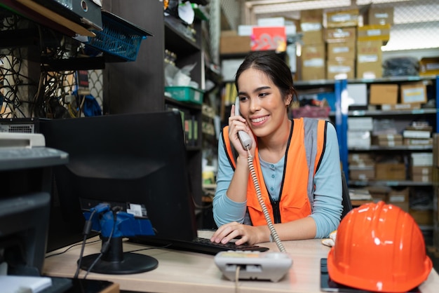 Lachende Aziatische jonge vrouw die telefonisch praat met de klant op het kantoor van de magazijnfabriek