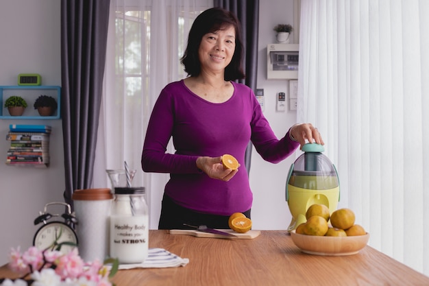 Lachende Aziatische ouderen maken sinaasappelsap met een blender.