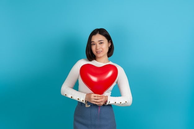 lachende Aziatische vrouw houdt een rode hartvormige ballon in de buurt van haar borst