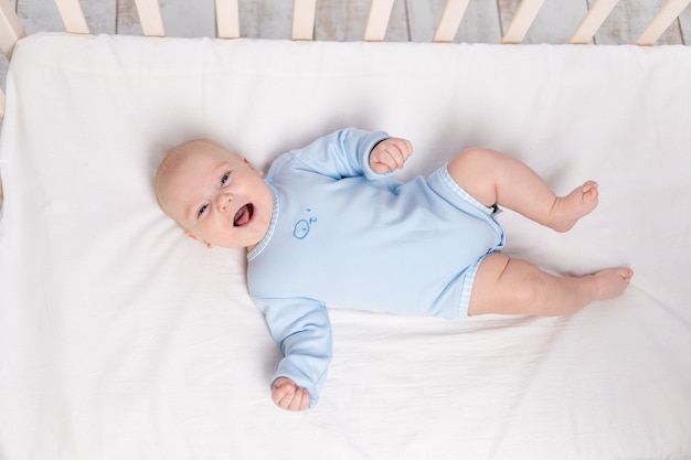 Lachende baby ligt in de wieg, schattige kleine jongen van zes maanden ligt in de kinderkamer op het bed en lacht