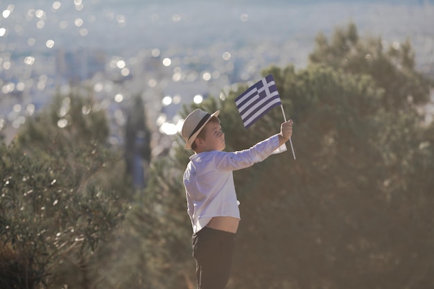 Lachende baby peuter jongen met een vlag van Griekenland op de achtergrond van de stad Independence Day Flag Day