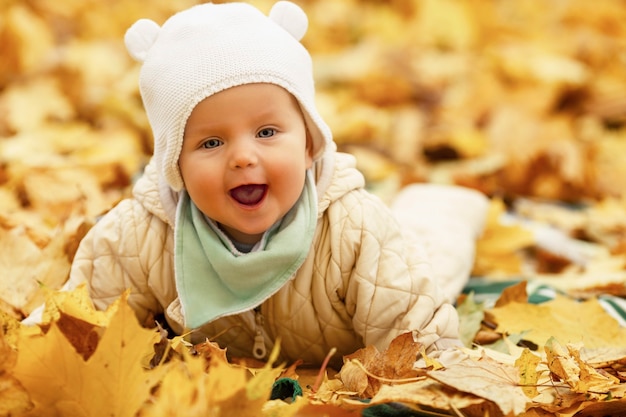 Lachende baby van 6 maanden oud ligt in een herfstpark op gevallen gele esdoornbladeren. Detailopname.