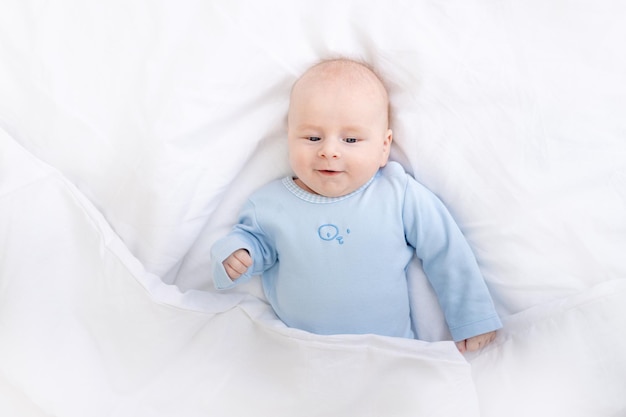 Lachende babyjongen op het bed onder de deken gezonde slaap baby