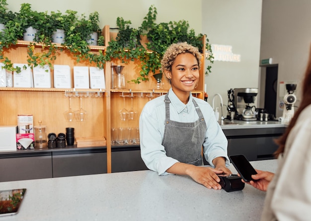 Lachende barista in schort die betaling ontvangt van een klant in een coffeeshop aan de balie