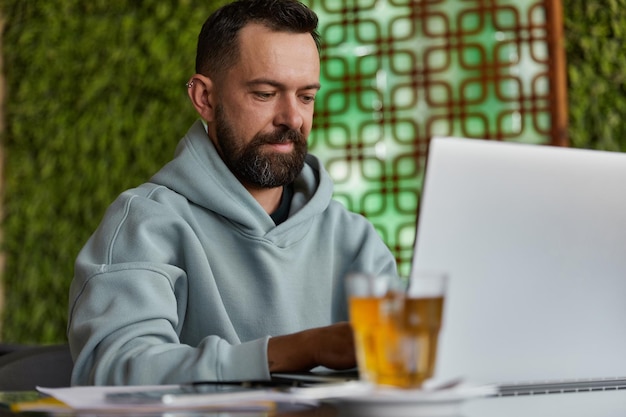 Lachende bebaarde man in casual kleding in café met behulp van laptop