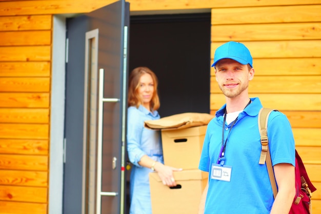 Foto lachende bezorger in blauw uniform die pakketdoos levert aan de ontvanger koeriersdienstconcept lachende bezorger in blauw uniform