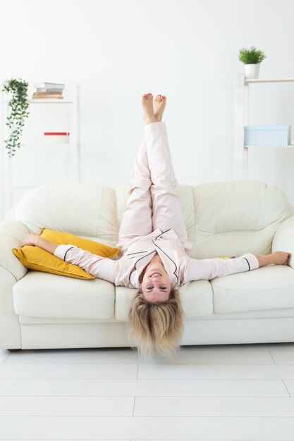 Lachende blonde vrouw zittend op comfortabele coach in woonkamer in pyjama homewear en vrije tijd vakantie thuis concept