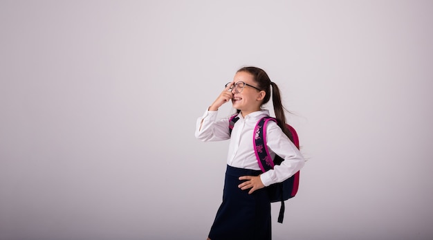 Lachende brunette schoolmeisje in uniform en bril op een witte achtergrond met een plek voor tekst