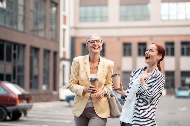 Lachende collega's. Twee elegante knappe blanke collega's die lachen terwijl ze buiten staan met papieren kopjes koffie