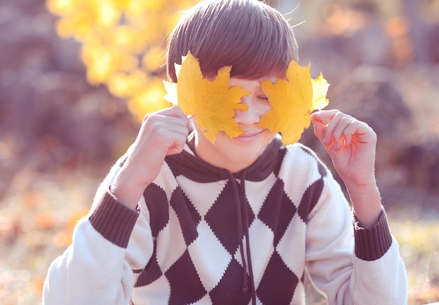 Lachende gelukkige tiener jongen 12-14 jaar oud spelen met gele bladeren in park buiten. Herfstseizoen