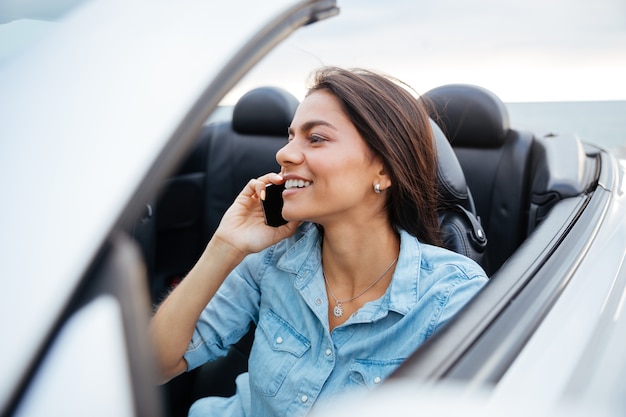 Lachende gelukkige vrouw auto rijden en praten op mobiele telefoon
