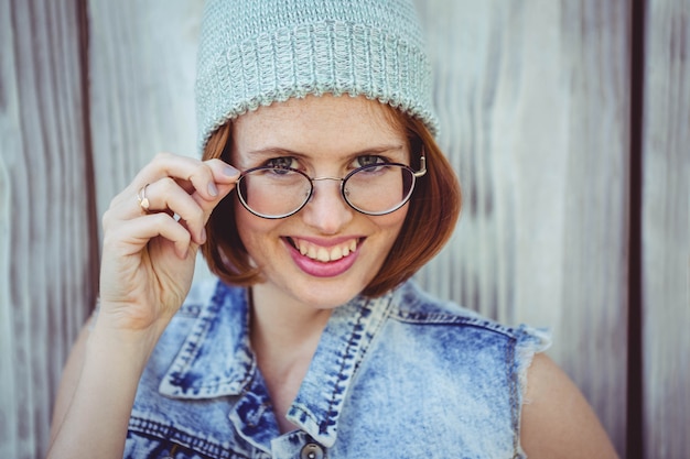 lachende hipster vrouw in een muts en een bril tegen een houten baackkground