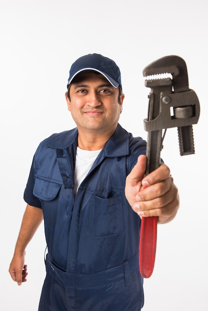 Lachende indiase loodgieter met waterpomptang of sanitair spanner, gekleed in een blauw uniform met dop met duimen omhoog. geïsoleerd