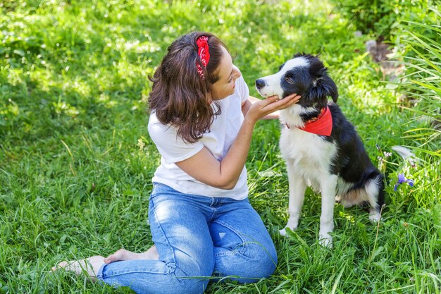 Lachende jonge aantrekkelijke vrouw spelen met schattige puppy hondje Bordercollie in zomertuin of stadspark buiten