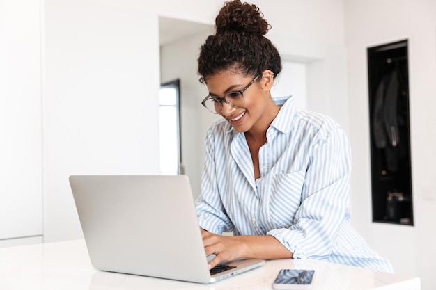 lachende jonge afrikaanse vrouw die thuis op een laptop aan tafel werkt