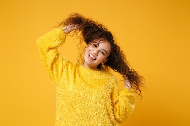 Lachende jonge afro-amerikaanse meisje in bont trui poseren geïsoleerd op geel oranje achtergrond studio portret. mensen oprechte emoties levensstijl concept. bespotten kopie ruimte. plezier hebben met het vasthouden van haar.