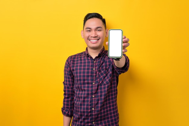 Lachende jonge Aziatische man met smartphone met leeg scherm geïsoleerd op gele achtergrond Reclame voor nieuwe mobiele app mockup concept