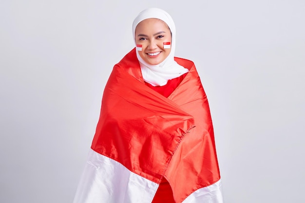 Lachende jonge Aziatische moslimvrouw in rood wit tshirt vieren Indonesische onafhankelijkheidsdag met trots tonen vlag Indonesisch geïsoleerd op witte achtergrond