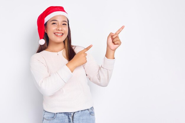Lachende jonge Aziatische vrouw in een kerstman hoed wijzende vingers naar lege kopie ruimte geïsoleerd op witte achtergrond viering Kerst vakantie en Nieuwjaar concept