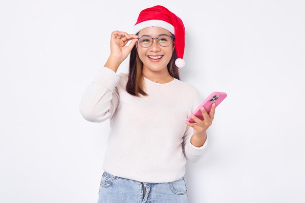 Lachende jonge Aziatische vrouw in een kerstmuts met smartphone die geweldig nieuws krijgt geïsoleerd op witte achtergrond viering Kerst vakantie en Nieuwjaar concept