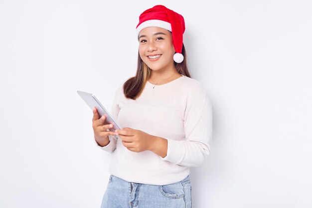 Lachende jonge Aziatische vrouw met kerstmuts met behulp van digitale tablet geïsoleerd op witte achtergrond Indonesische mensen vieren kerst concept