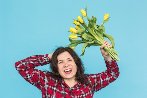 Lachende jonge blanke vrouw met boeket tulpen op blauwe achtergrond.