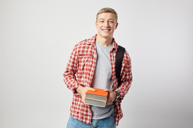 lachende jonge blonde man met rugzak houdt boeken in zijn handen