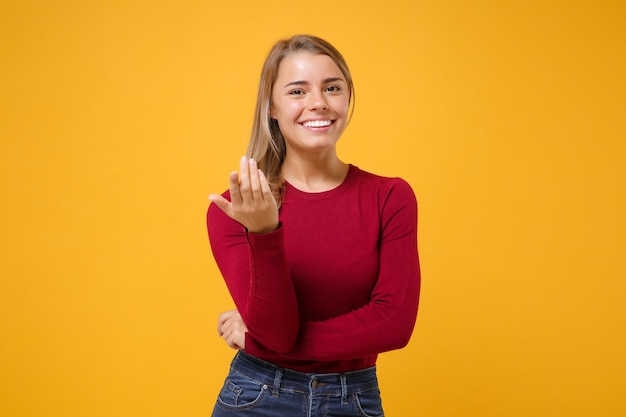 Lachende jonge blonde vrouw meisje in casual kleding poseren geïsoleerd op geeloranje achtergrond in de studio. mensen levensstijl concept. mock up kopie ruimte. doe een oproepgebaar zoals zegt, kom hier naar mij toe.