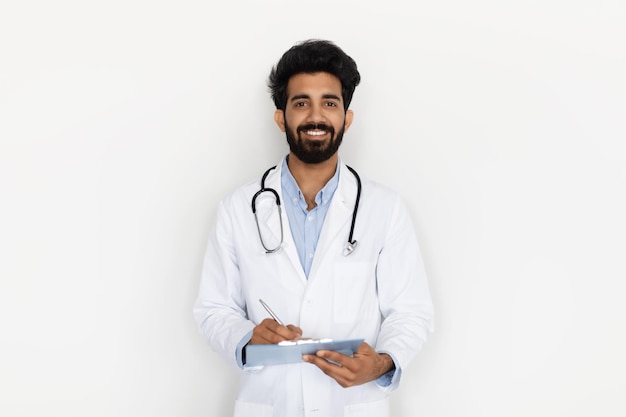 Lachende jonge Indiase arts die zich voordeed op witte achtergrond