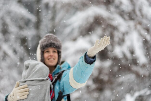 Lachende jonge moeder met haar baby in een draagzak, sneeuwvlokken vangen terwijl ze buiten staat op een besneeuwde winterdag.