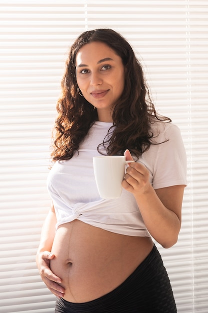 Lachende jonge mooie zwangere vrouw haar buik aan te raken en vreugde. Concept van positieve en aangename gevoelens tijdens het wachten op de baby.