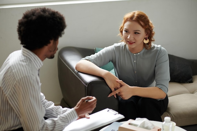 Foto lachende jonge vrouw die met haar psycholoog praat tijdens therapiesessie