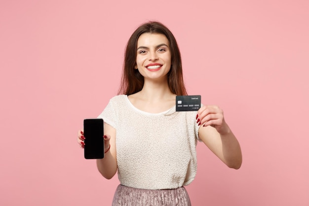 Lachende jonge vrouw in casual lichte kleding poseren geïsoleerd op pastel roze muur achtergrond. Mensen levensstijl concept. Bespotten kopie ruimte. Mobiele telefoon vasthouden met een leeg leeg scherm creditcard bankkaart.