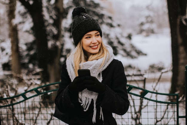 Lachende jonge vrouw in gezellige kleding met behulp van mobiele telefoon op winterdag