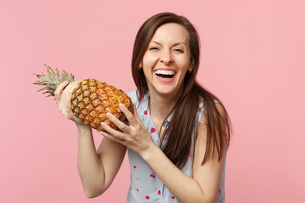 Lachende jonge vrouw in zomerkleren met in handen vers rijp ananasfruit geïsoleerd op roze pastelmuurachtergrond in studio. Mensen levendige levensstijl ontspannen vakantie concept. Bespotten kopie ruimte.