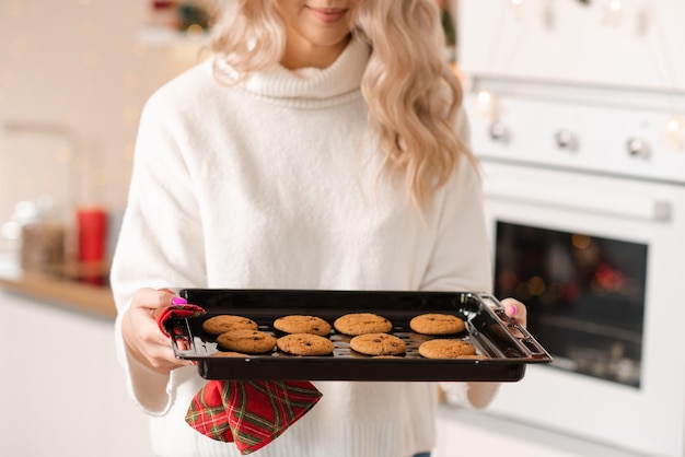 Lachende jonge vrouw met bakplaat met lekkere gekookte koekjes vers uit de oven thuis in de keuken Gelukkige moeder maakt kerstgebak voor het ontbijt Goedemorgen