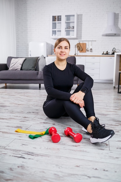 Lachende jonge vrouw trainen met elastische band thuis fitnesstraining. Gezond levensstijlconcept. Thuis sporten tijdens quarantaine