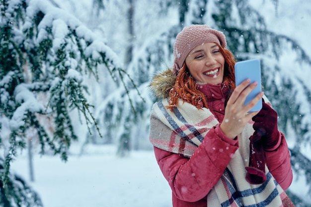 Lachende jonge vrouw typen op telefoon op koude winterdag