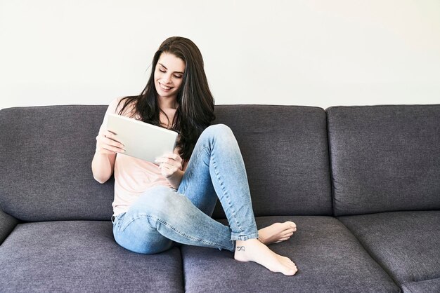 Lachende jonge vrouw zittend op de bank met tablet