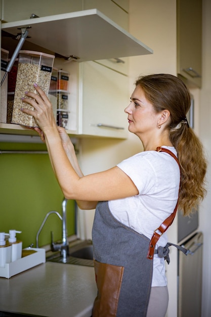 Foto lachende jonge vrouwelijke huisvrouw die zich voordeed tijdens algemene schoonmaak opruimen in de keuken van de kast