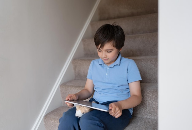 Lachende jongen zittend op de trap genieten van het spelen van online game op digitale tabletcomputer Happy Kid met behulp van applicaties of websurfinformatie voor huiswerk Kinderen verslaafd aan technologie