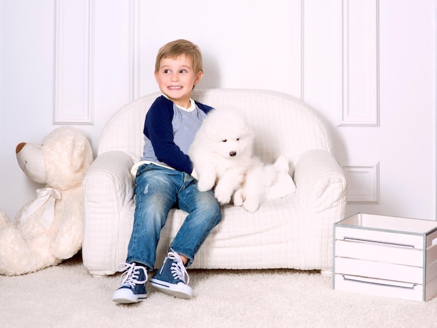 Lachende kleine drie jaar oude jongen spelen met witte puppy van samojeed in studio