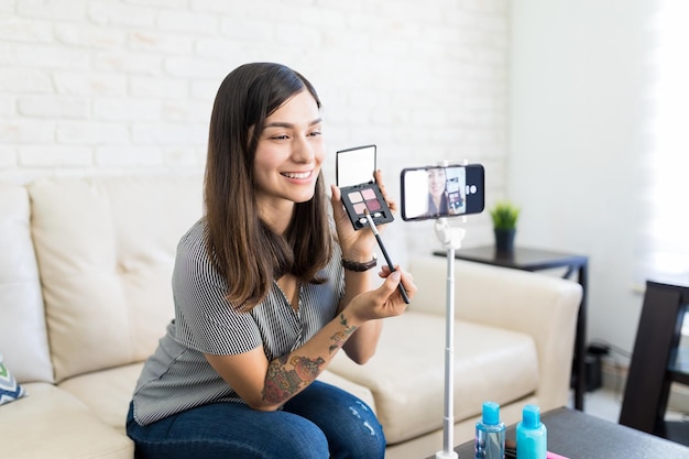 Lachende Latijns-beïnvloeder die make-upvideo opneemt voor beautyblog op smartphone