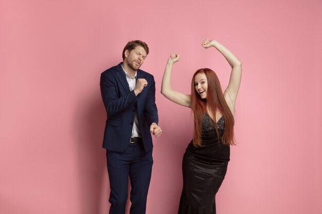 Lachende man en vrouw die samen dansen. Valentijnsdagviering, gelukkig Kaukasisch paar op koraalachtergrond. Concept van menselijke emoties, gezichtsuitdrukking, liefde, relaties, romantische vakanties.