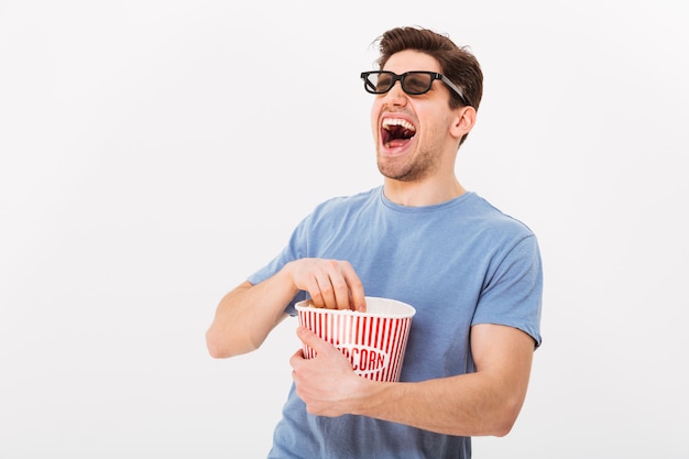 Lachende man in t-shirt en 3d bril popcorn eten uit emmer en weg kijken over grijze muur