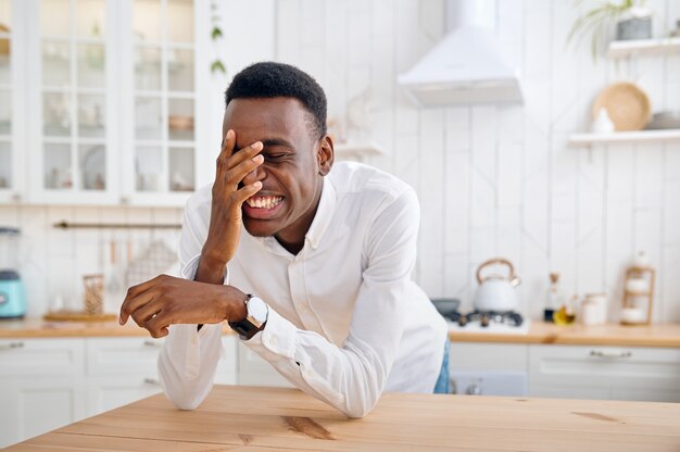 Lachende man zit aan de balie in de keuken. Vrolijke mannelijke persoon poseert 's ochtends thuis aan tafel