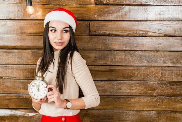 lachende meisje in een kerstmuts op houten achtergrond met klok